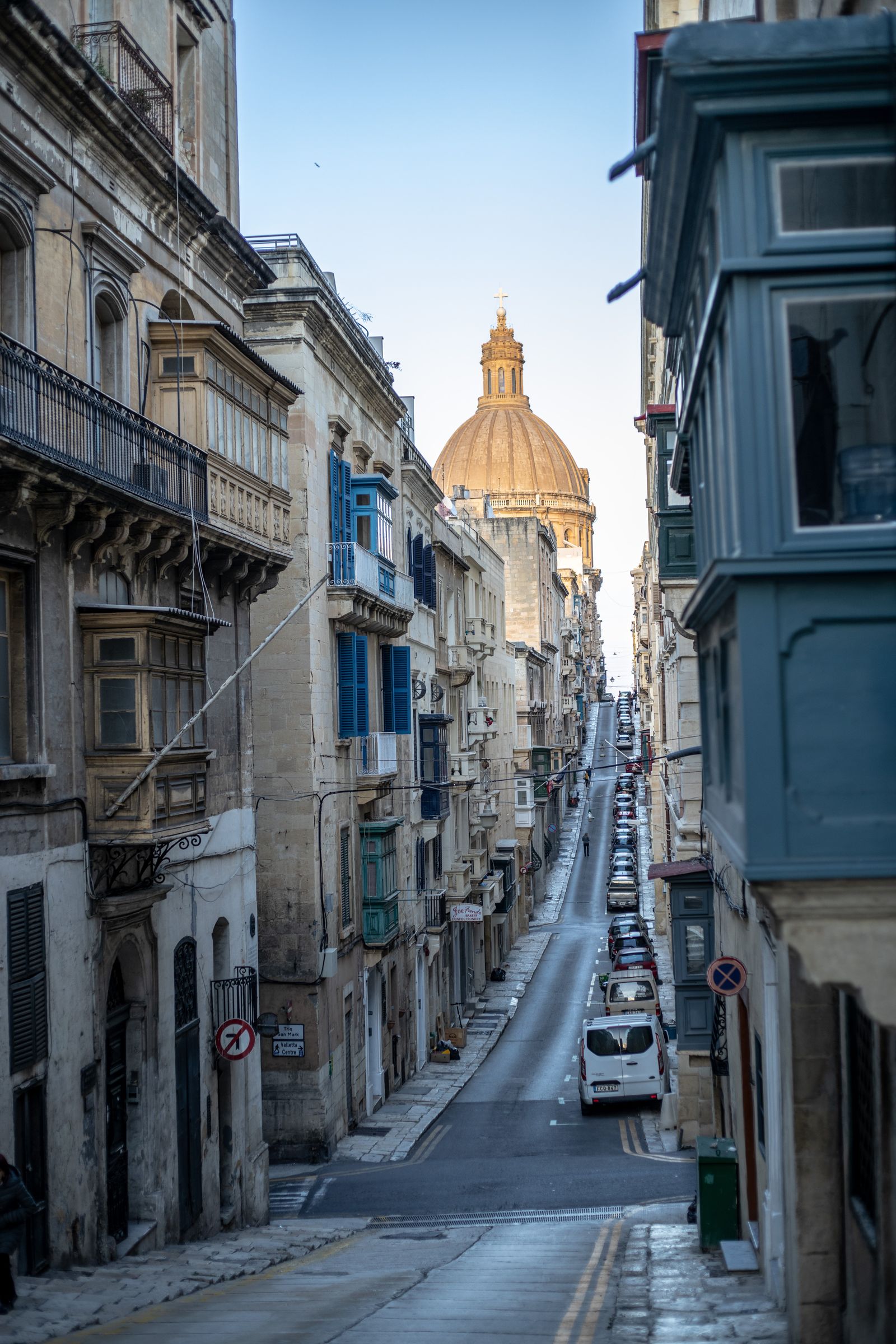 A narrow Valletta street of limestone facades leading toward a church dome